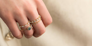 Woman wearing four 14k gold rings on her hand. A  Diamond Distance Band, Petite Diamond Distance Band, and Sapphire Sapling Ring