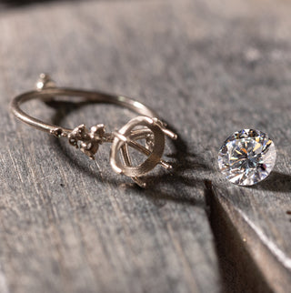 A Melanie Casey Snowdrift Ring in Round Cut Diamond is shown being worked on at the jeweler's bench, with the stone sitting aside the ring setting during this step in the process.