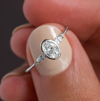 Photo features a model holding up the Bezel Engagement Circlet Ring in oval cut and white gold with her fingers.