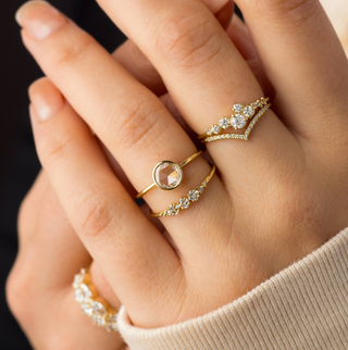 Photo features a model wearing the Caldera Bezel Engagement Ring on her ring finger paired with several other Melanie Casey rings.