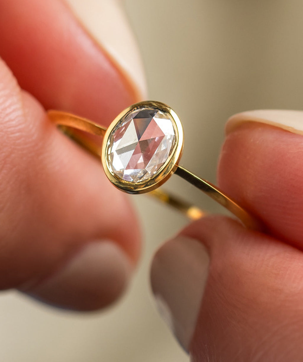 Photo shows a Melanie Casey Bezel Rose Cut Engagement Ring in Yellow Gold held between two hands.