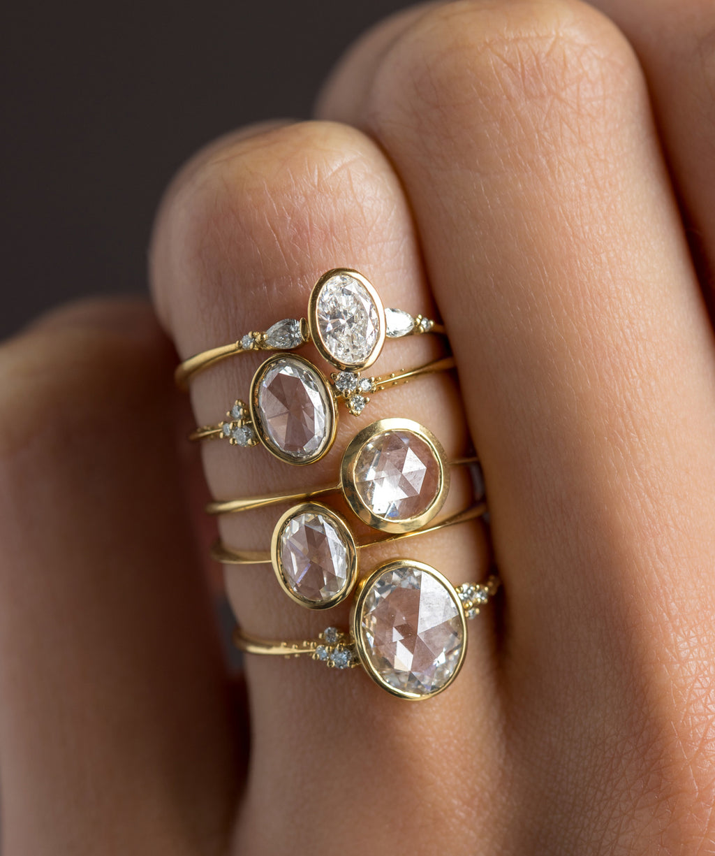 Photo features Melanie Casey Bezel Rose Cut Engagement Rings in Yellow Gold being worn stacked together on someone's hand.