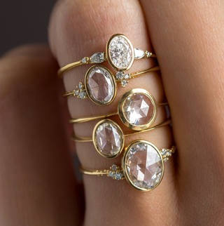 Photo features Melanie Casey Bezel Rose Cut Engagement Rings in Yellow Gold being worn stacked together on someone's hand.