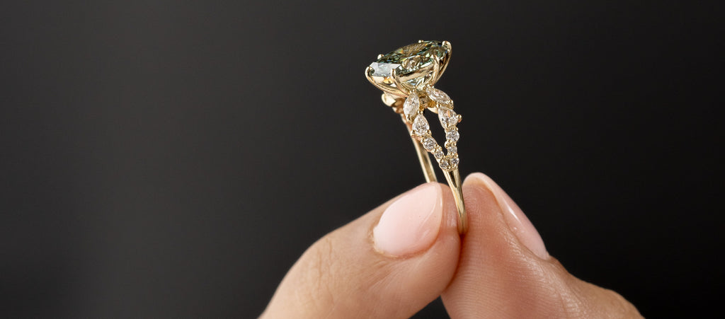 Photo features a model holding a Melanie Casey Green Diamond Prophecy Ring, showing it's side profile.