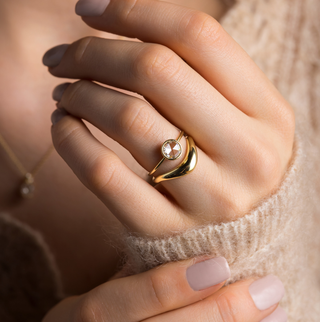 Photo features the Caldera Bezel Engagement Ring in Round Rose Cut on a model's hand, as she touches her hand and wrist with her other other hand. She has paired the Caldera Ring with an Amplify Band in yellow gold underneath.