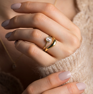 Photo features the Caldera Bezel Engagement Ring in Round Rose Cut on a model's hand, as she touches her hand and wrist with her other other hand. She has paired the Caldera Ring with an Amplify Band in yellow gold underneath.